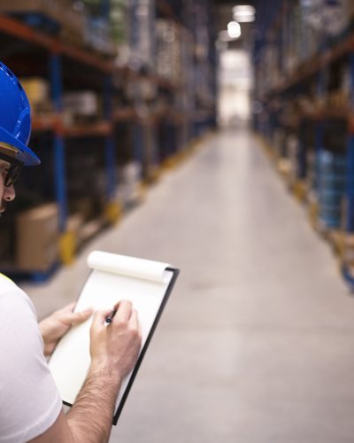 Factory worker holding clipboard and checking inventory of warehouse storage department.