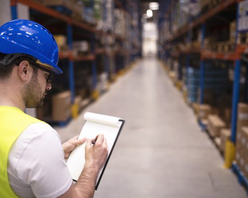 Factory worker holding clipboard and checking inventory of warehouse storage department.